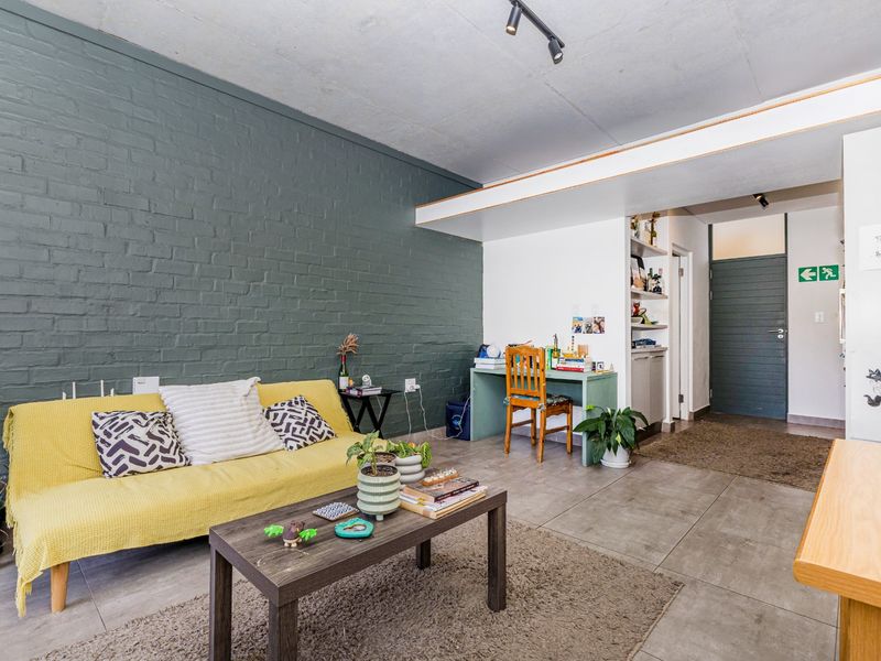 A contemporary living area featuring an exposed painted brick feature wall, large format floor tiles, and modern track lighting.
