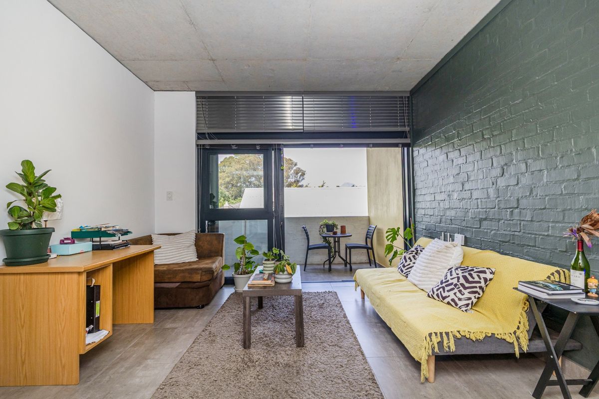 A modern living room featuring an exposed concrete ceiling, a dark painted brick feature wall, and large sliding doors leading to a private balcony.