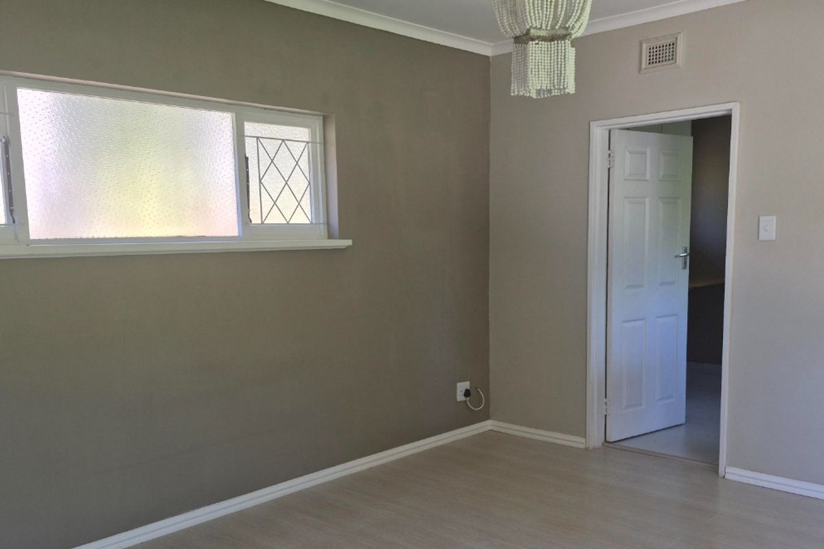 A bright, empty bedroom featuring neutral walls, laminate flooring, and a classic panelled door, offering a clean canvas for personalization.