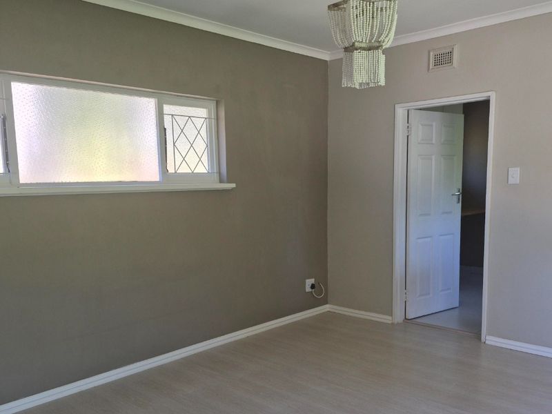 A bright, empty bedroom featuring neutral walls, laminate flooring, and a classic panelled door, offering a clean canvas for personalization.