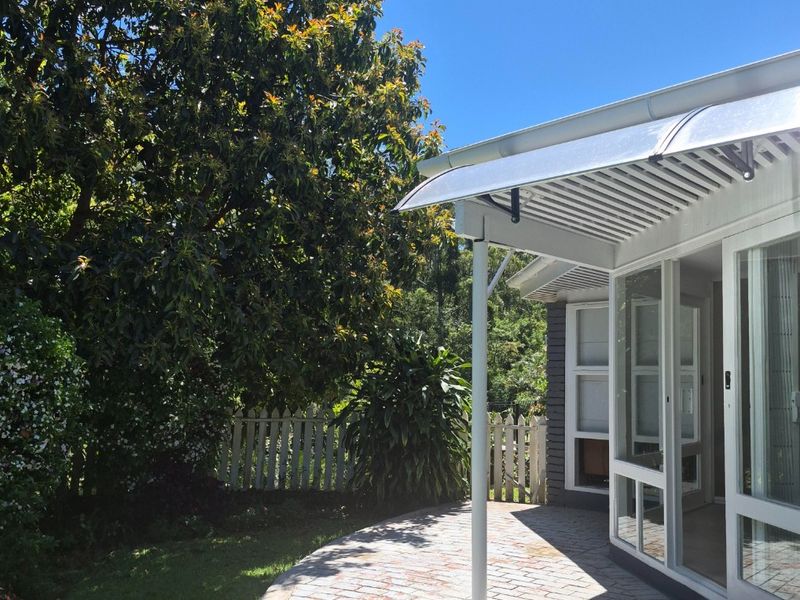 A well-maintained brick paved patio area featuring a protective polycarbonate awning and direct access to the interior through sliding glass doors.
