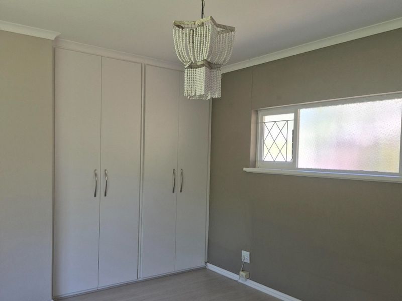 A bright, empty bedroom featuring neutral walls, laminate flooring, built-in cupboards, and a decorative leaded glass window.