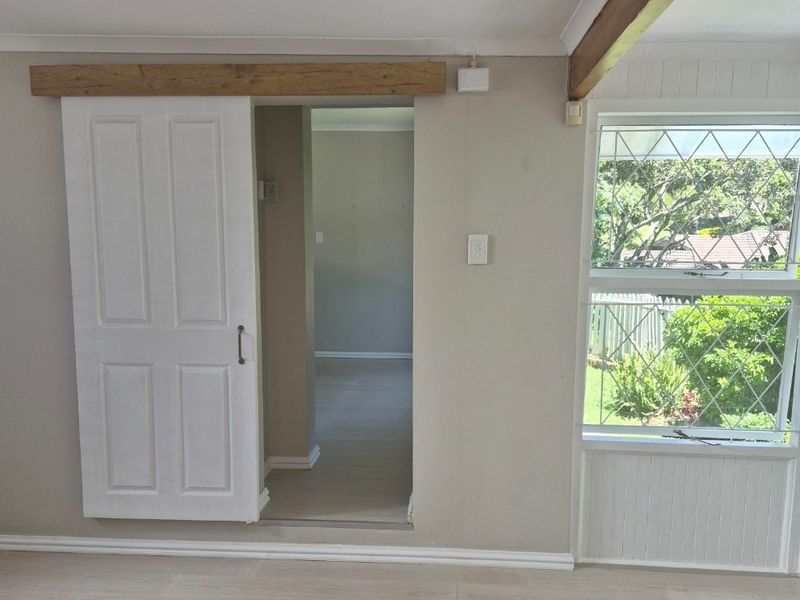Bright living area featuring light laminate flooring, an exposed timber ceiling beam, and a sliding barn door leading to an adjacent room.