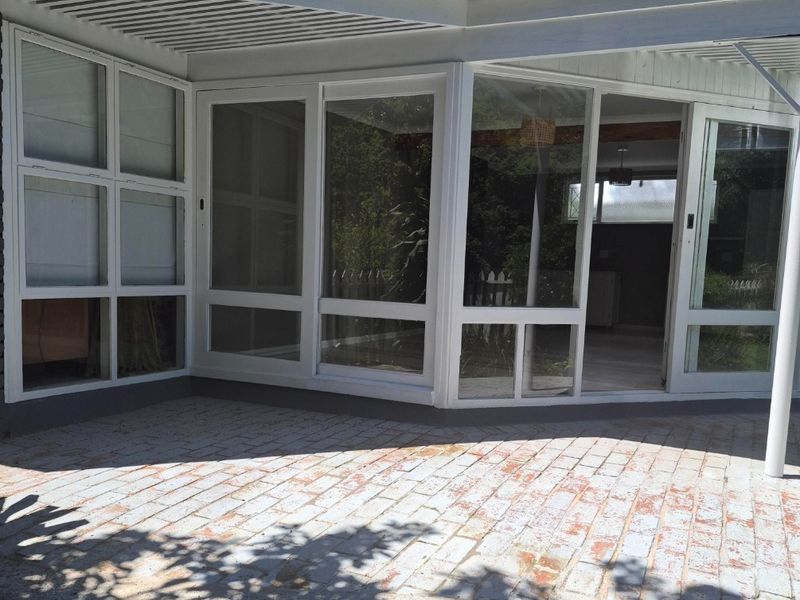 A covered outdoor patio area featuring brick paving, large glass sliding doors, and a prominent brick chimney, offering a transition to the interior space.