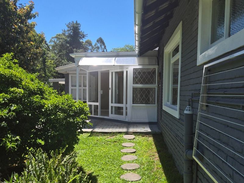 A view of the rear exterior of the cottage, featuring a paved patio area, glass doors, and a landscaped garden path.