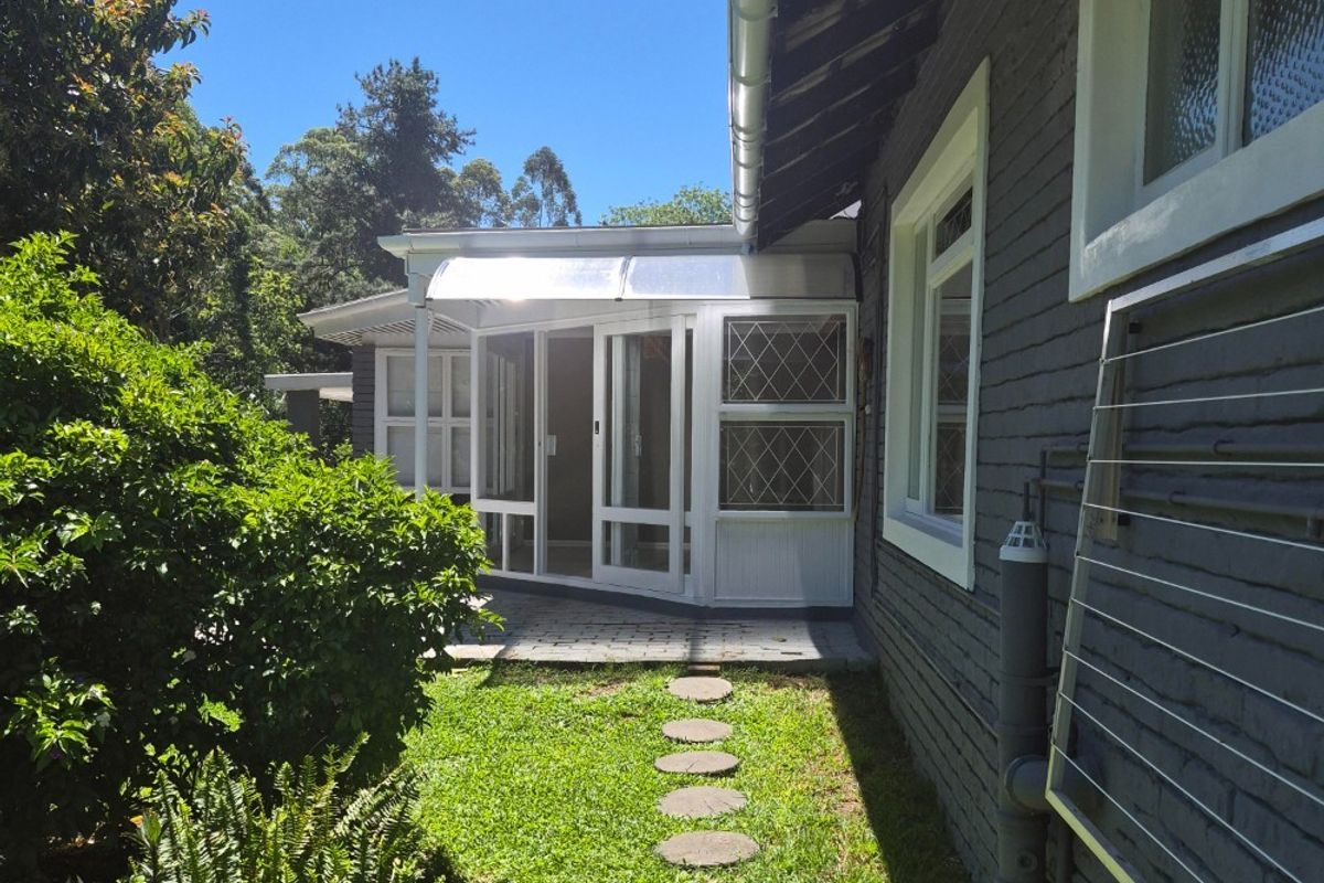 A view of the rear exterior of the cottage, featuring a paved patio area, glass doors, and a landscaped garden path.