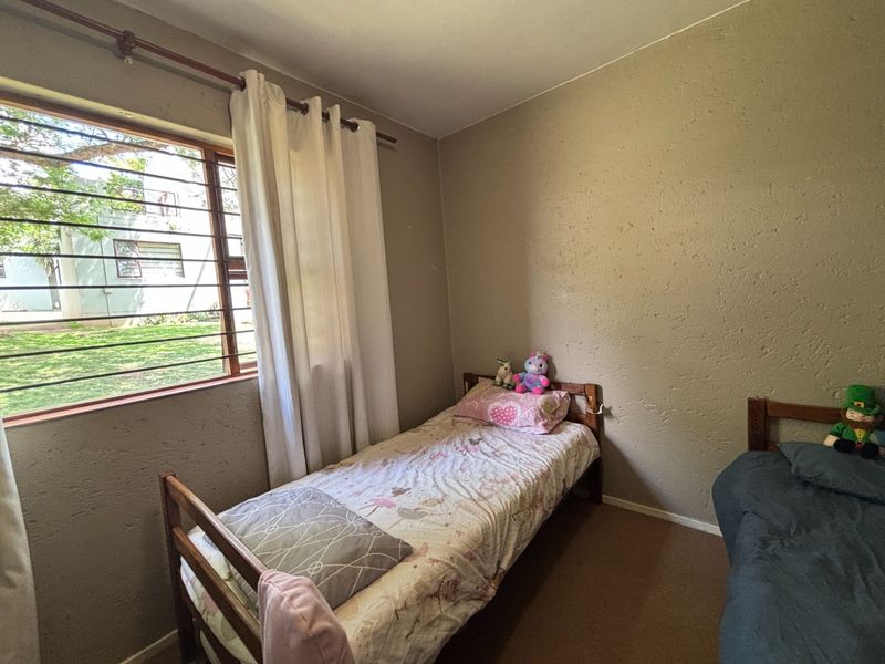 A functional bedroom featuring a window with security bars and neutral textured wall finishes.