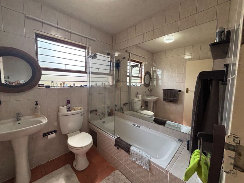 A functional bathroom featuring a pedestal basin, toilet, and a built-in bathtub with a glass shower screen, finished with full-height wall tiling.