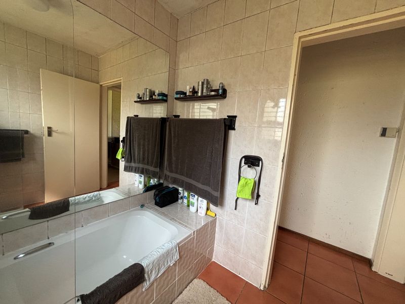A dated bathroom featuring a built-in bathtub, tiled walls and flooring, and a large wall-mounted mirror.
