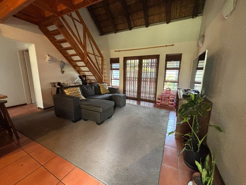 Spacious living room featuring a unique thatched roof, wooden staircase, and tiled flooring with direct access to the outdoor area through sliding security doors.