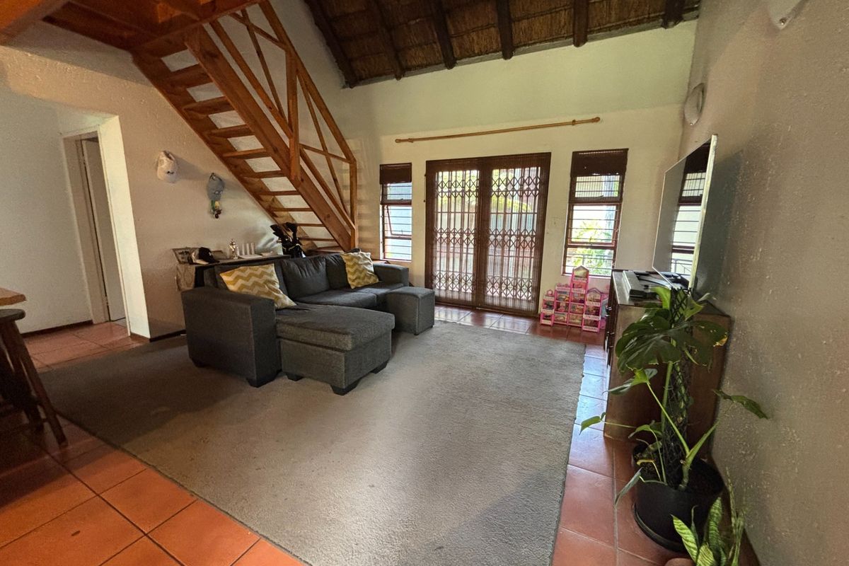 Spacious living room featuring a unique thatched roof, wooden staircase, and tiled flooring with direct access to the outdoor area through sliding security doors.