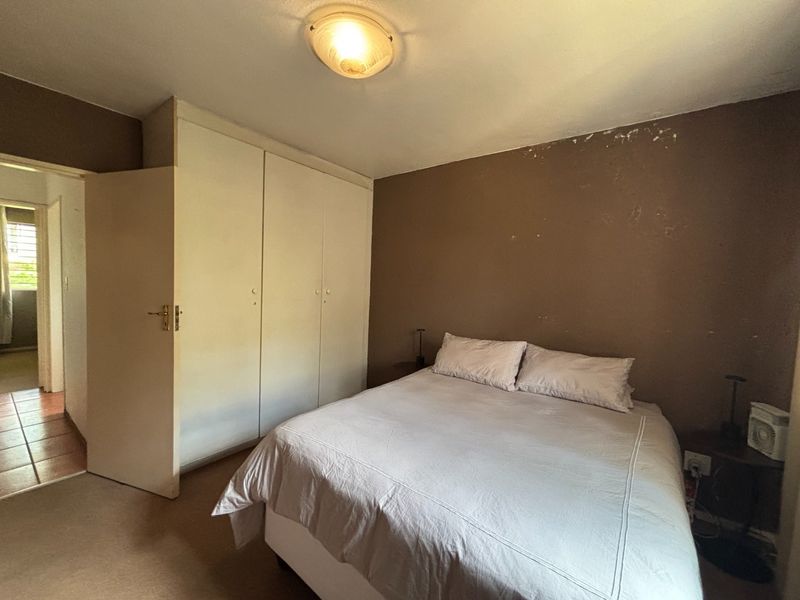 A bedroom featuring a built-in wardrobe and ceiling lighting, currently showing signs of wear on the wall finishes.
