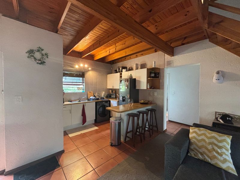 Open plan kitchen area featuring exposed timber beam ceilings, tiled flooring, and a functional breakfast bar, creating a warm and inviting living space.