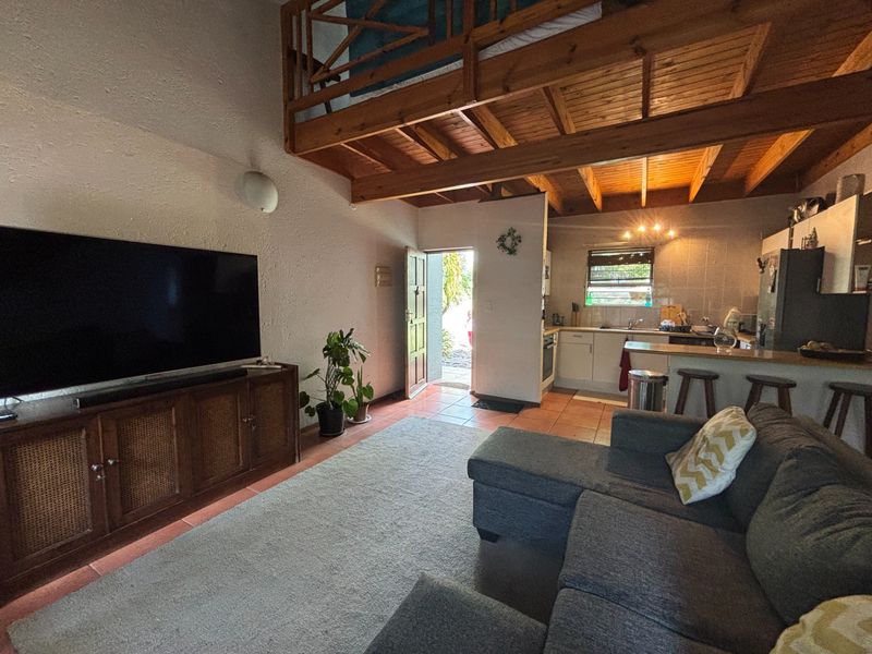 Open plan living area featuring a mezzanine level with timber ceiling, tiled floors, and an integrated kitchen with functional cabinetry and built-in appliances.