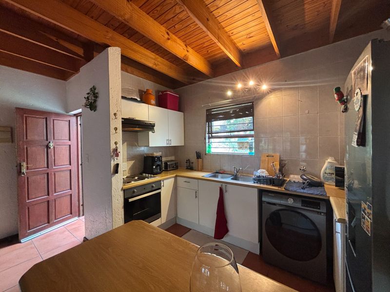 Functional kitchen featuring exposed timber beam ceilings, built-in oven, hob, extractor fan, and tiled splashback with integrated laundry appliance space.