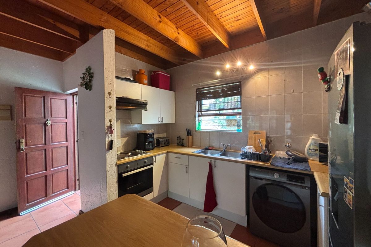 Functional kitchen featuring exposed timber beam ceilings, built-in oven, hob, extractor fan, and tiled splashback with integrated laundry appliance space.