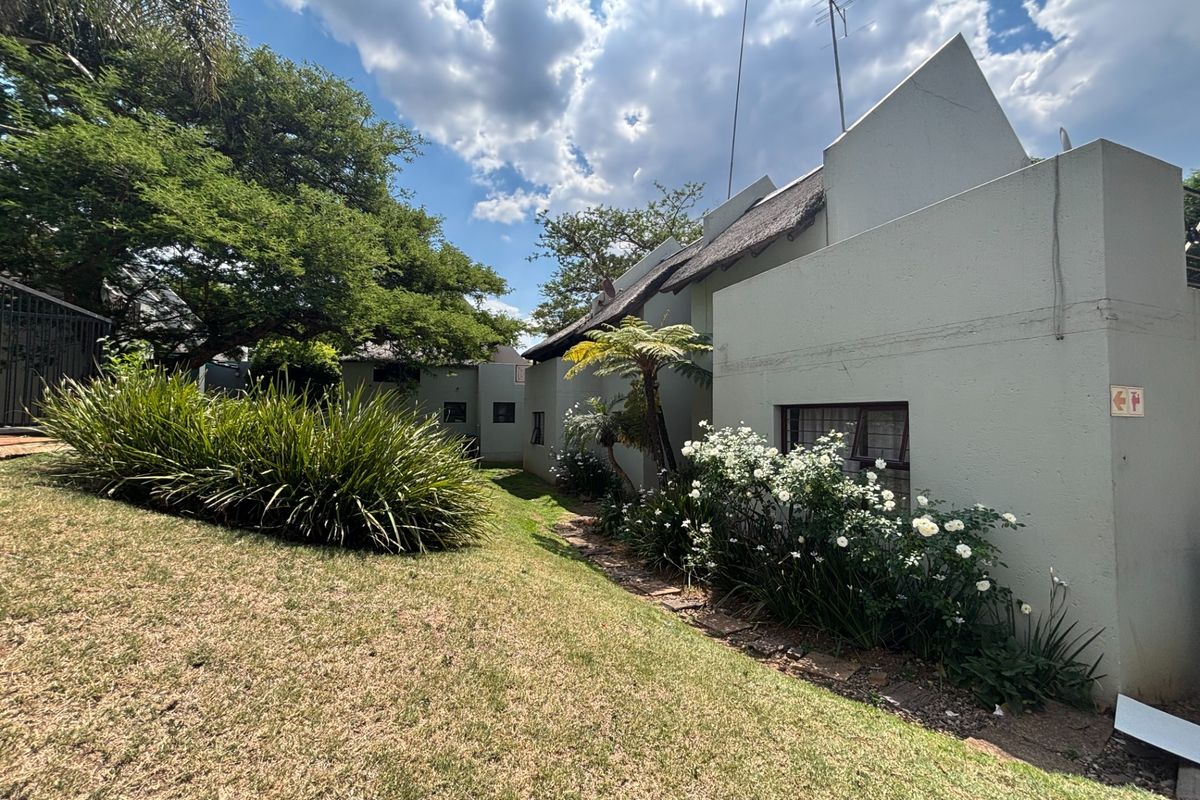 A view of the rear exterior of the property featuring plastered walls, a traditional thatched roof, and a well-maintained garden area.
