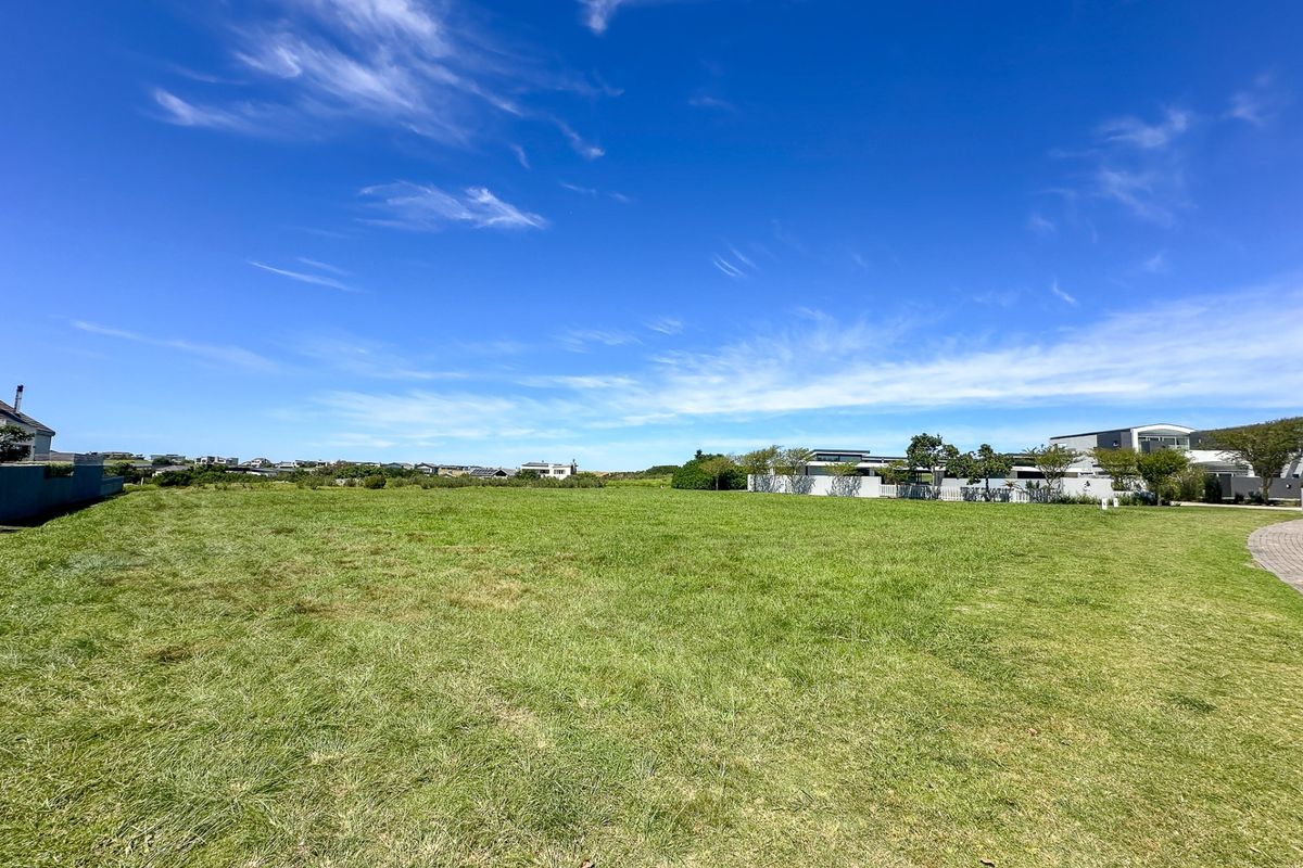 A wide, open residential vacant land plot featuring a well-maintained grass lawn and surrounding boundary walls in a quiet neighborhood setting.