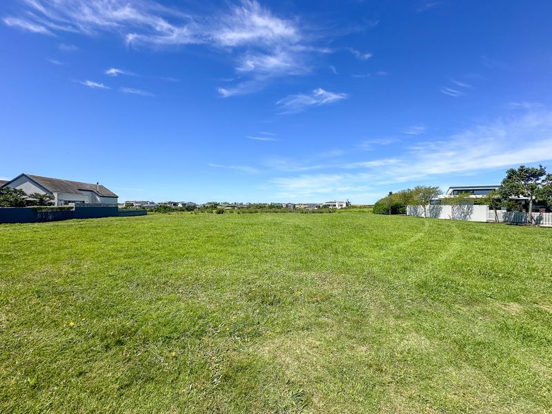 A spacious, level residential vacant land plot featuring well-maintained grass and surrounding boundary walls in a quiet neighborhood setting.