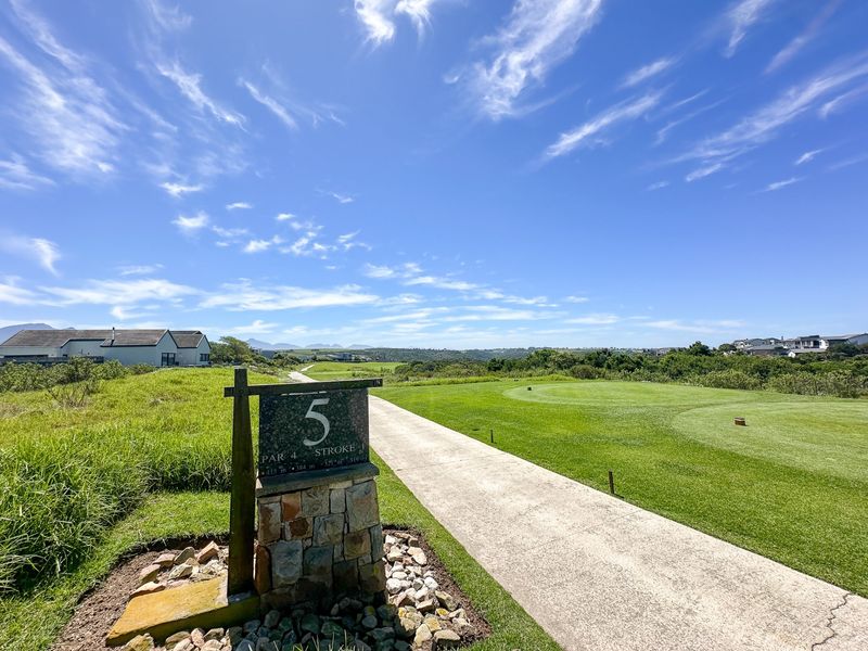 A scenic view of a golf course fairway with a paved pathway and surrounding natural landscape.