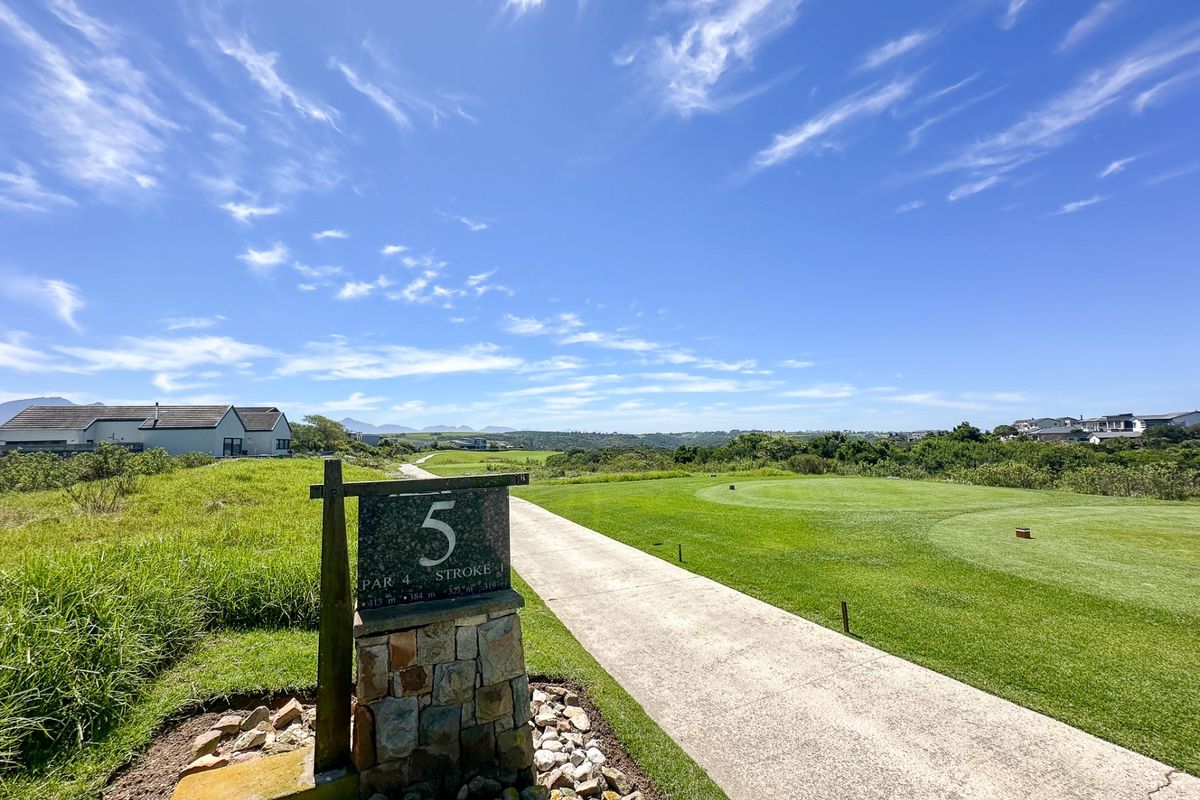 A scenic view of a golf course fairway with a paved pathway and surrounding natural landscape.