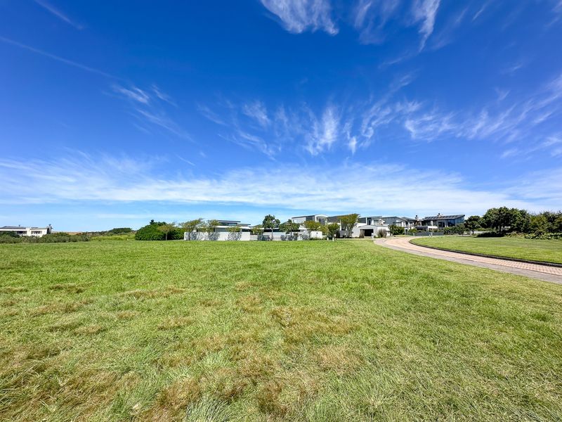 A wide-angle view of a vacant residential plot featuring a well-maintained lawn and a paved driveway leading towards neighboring properties.