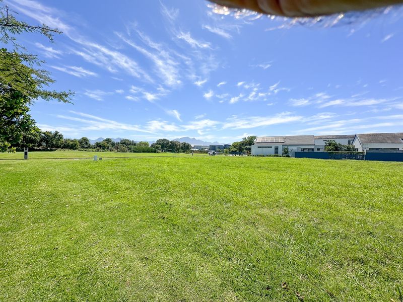 A spacious, well-maintained residential plot featuring a large green lawn with distant mountain views and surrounding neighborhood infrastructure.