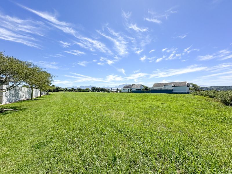 A spacious, well-maintained residential vacant plot featuring expansive green lawn and perimeter boundary walling with distant mountain views.