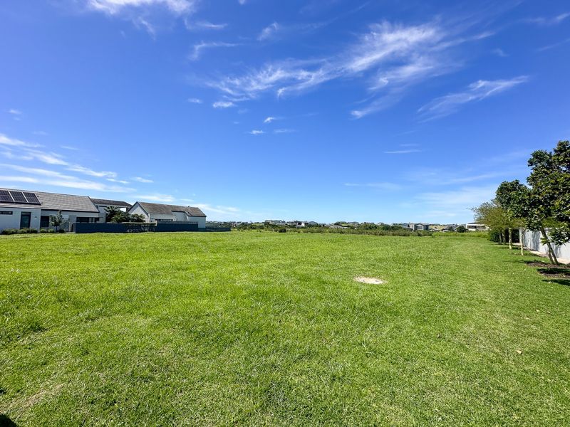 A wide, level residential vacant plot featuring a well-maintained grass lawn with surrounding neighborhood views.