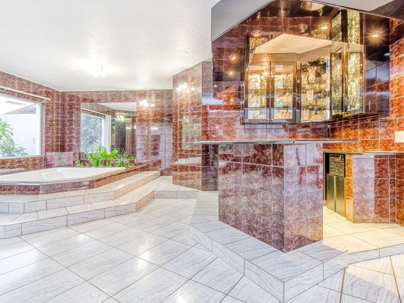 Unique entertainment space featuring a built-in bar with display cabinetry and a sunken jetted bathtub, finished with extensive decorative tiling.