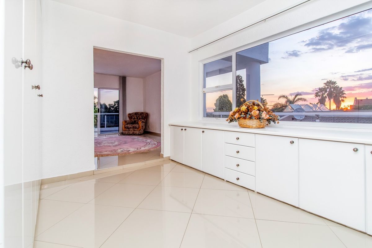 Bright and spacious living area featuring sleek built-in cabinetry, polished tiled flooring, and large windows offering scenic sunset views.