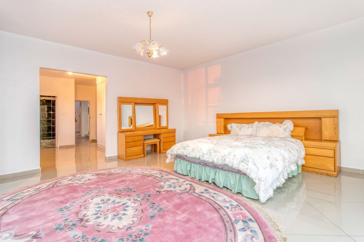 Spacious bedroom featuring built-in wooden cabinetry, including a headboard, bedside tables, and a vanity, complemented by polished tiled flooring.