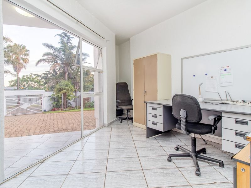 A functional home office space featuring tiled flooring and a large sliding glass door providing direct access to the outdoor patio area.
