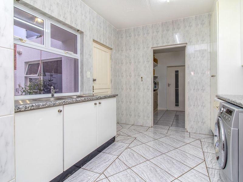 A functional laundry room featuring tiled walls and flooring, built-in cabinetry with granite countertops, and a stainless steel sink.