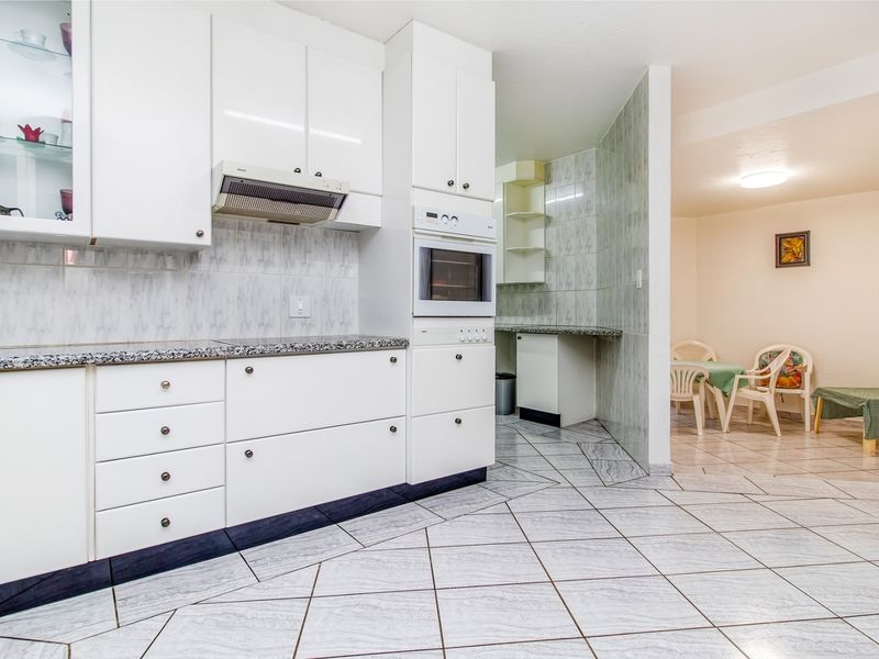 A functional kitchen featuring white cabinetry, granite countertops, built-in oven, extractor fan, and tiled flooring, with an adjacent dining area.