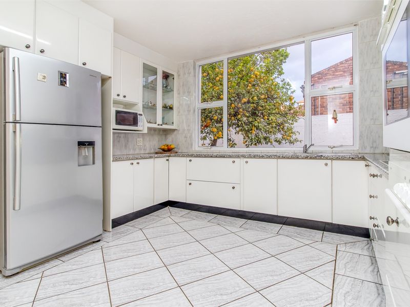 A bright, functional kitchen featuring white cabinetry, granite countertops, tiled flooring, and a large window overlooking the garden.