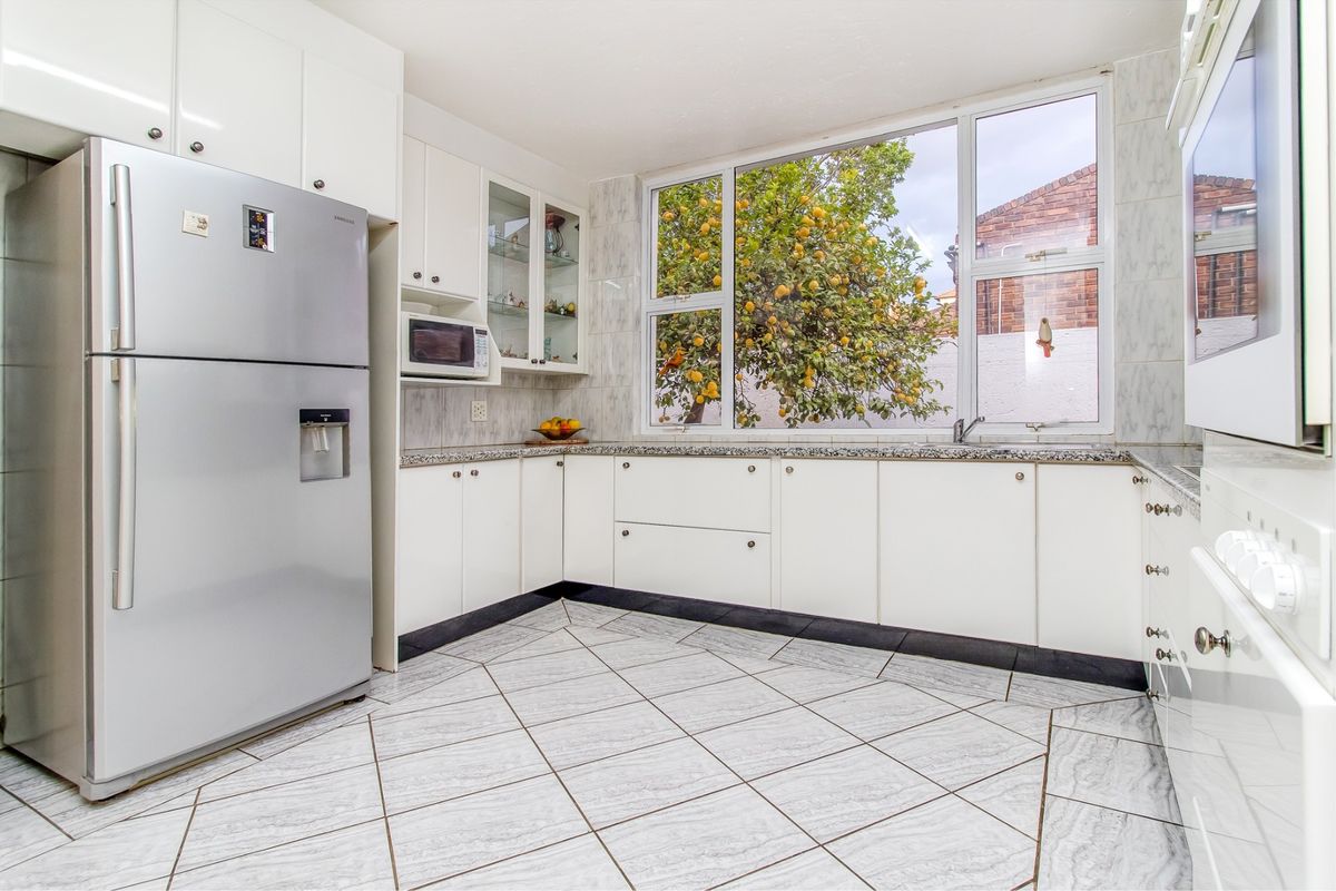 A bright, functional kitchen featuring white cabinetry, granite countertops, tiled flooring, and a large window overlooking the garden.