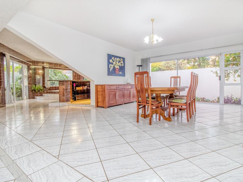 Spacious open-plan living and dining area featuring large format floor tiles, sliding glass doors to the garden, and a built-in tiled bar area.