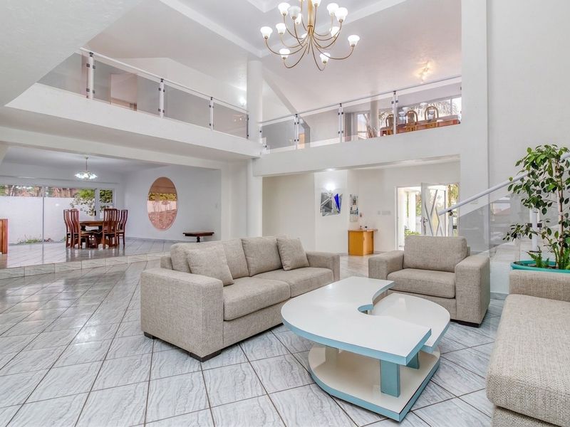 Spacious open-plan living area featuring a double-volume ceiling, mezzanine level with glass balustrades, tiled flooring, and elegant chandelier lighting.