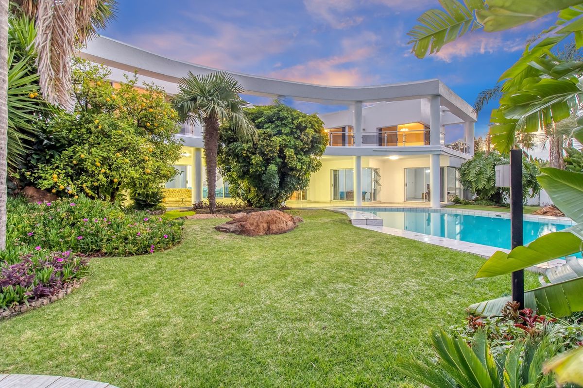 A beautifully landscaped rear garden featuring a swimming pool and a modern two-story home with a distinctive curved architectural facade and balcony.
