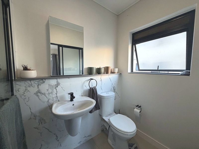 Modern bathroom featuring marble-look wall tiling, black tapware, a pedestal basin, and a functional awning window for natural ventilation.