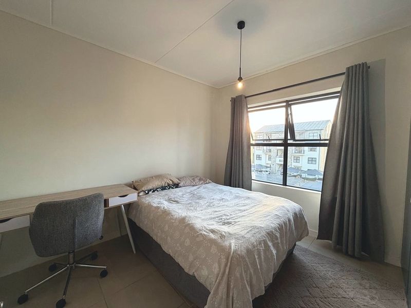 A functional bedroom featuring tiled flooring, a central pendant light, and an aluminium-framed window providing natural light.