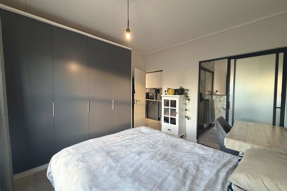 A well-lit bedroom featuring a large built-in wardrobe and a sliding glass door leading to an en-suite bathroom.