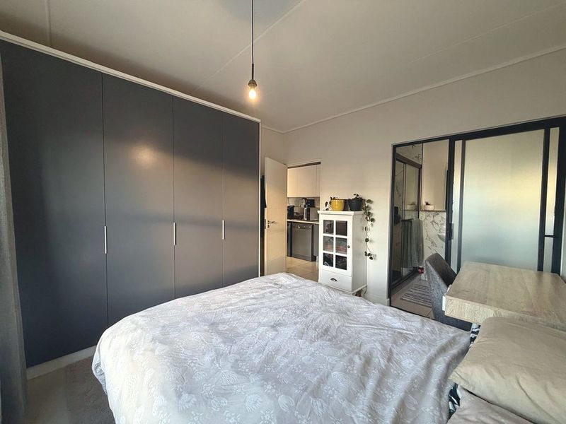 A well-lit bedroom featuring a large built-in wardrobe and a sliding glass door leading to an en-suite bathroom.