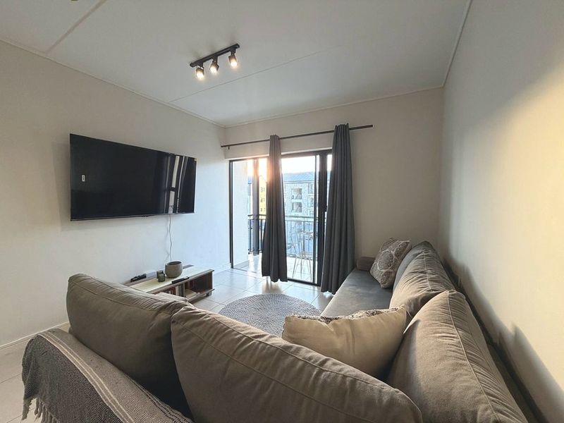 A comfortable living room featuring tiled flooring, modern track lighting, and a sliding glass door that provides direct access to a private balcony.