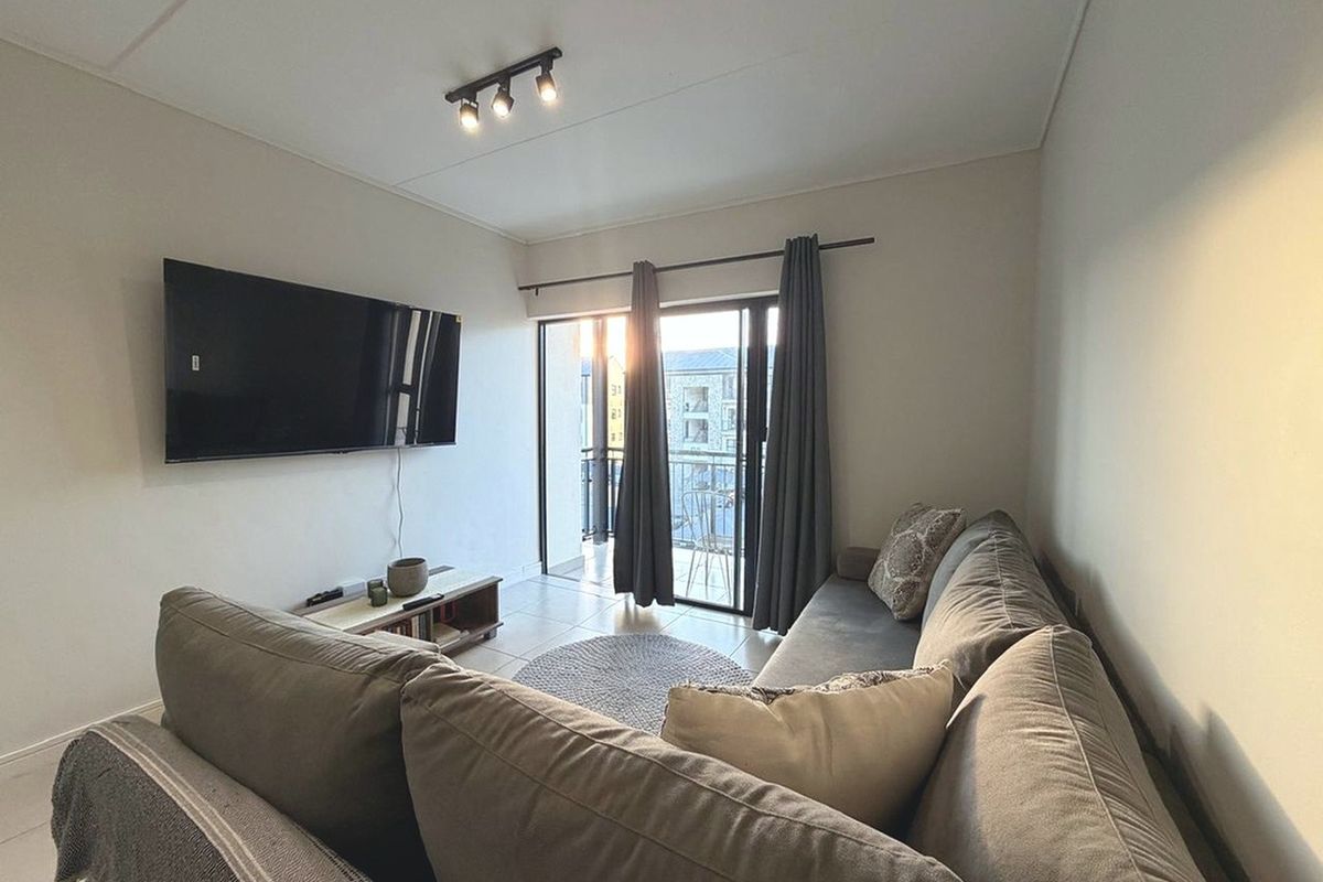 A comfortable living room featuring tiled flooring, modern track lighting, and a sliding glass door that provides direct access to a private balcony.