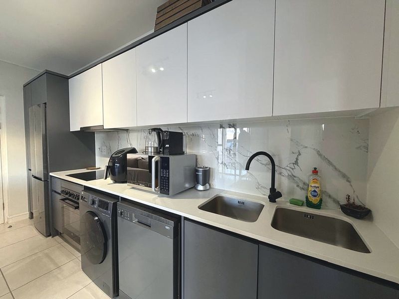 Modern kitchen featuring sleek white and grey cabinetry, stone countertops, marble-look splashback, and high-quality integrated appliances.