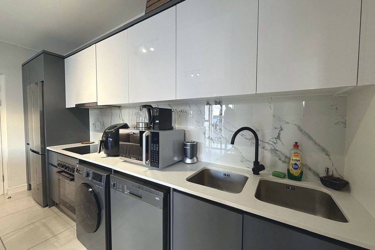 Modern kitchen featuring sleek white and grey cabinetry, stone countertops, marble-look splashback, and high-quality integrated appliances.