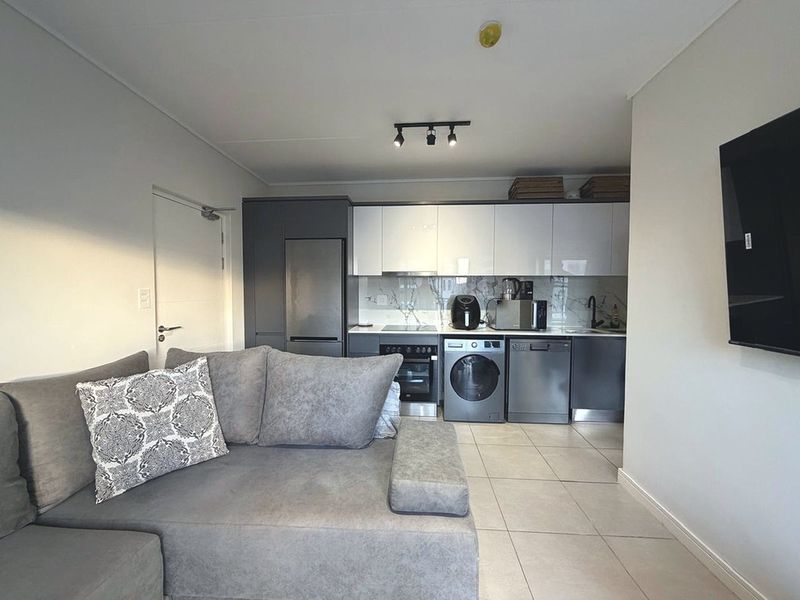 Modern open-plan living area featuring a sleek kitchen with high-gloss cabinetry, marble-look backsplash, and integrated appliances, complemented by neutral tiled flooring.