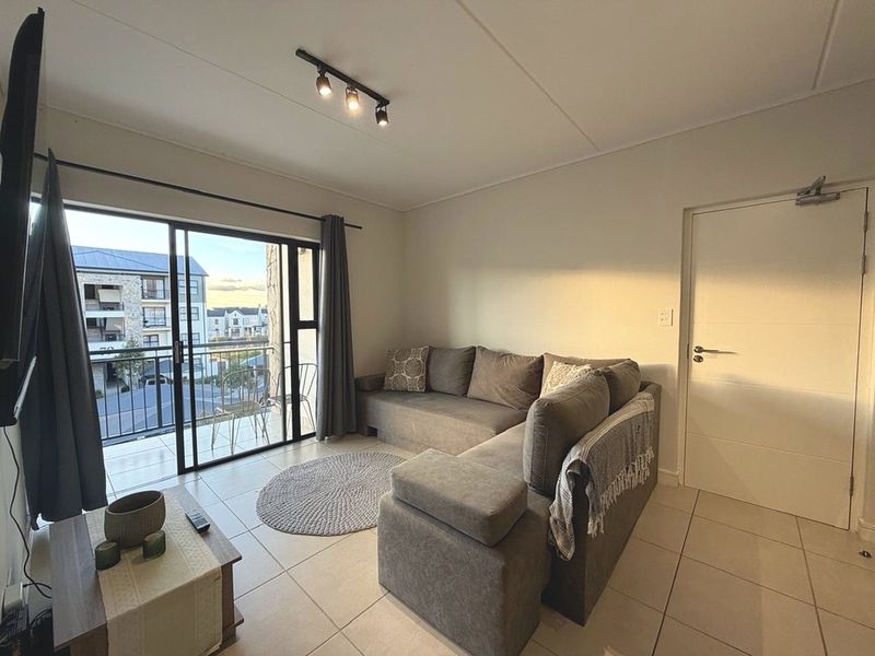 A bright living room featuring tiled flooring, modern track lighting, and a sliding glass door providing direct access to a private balcony.